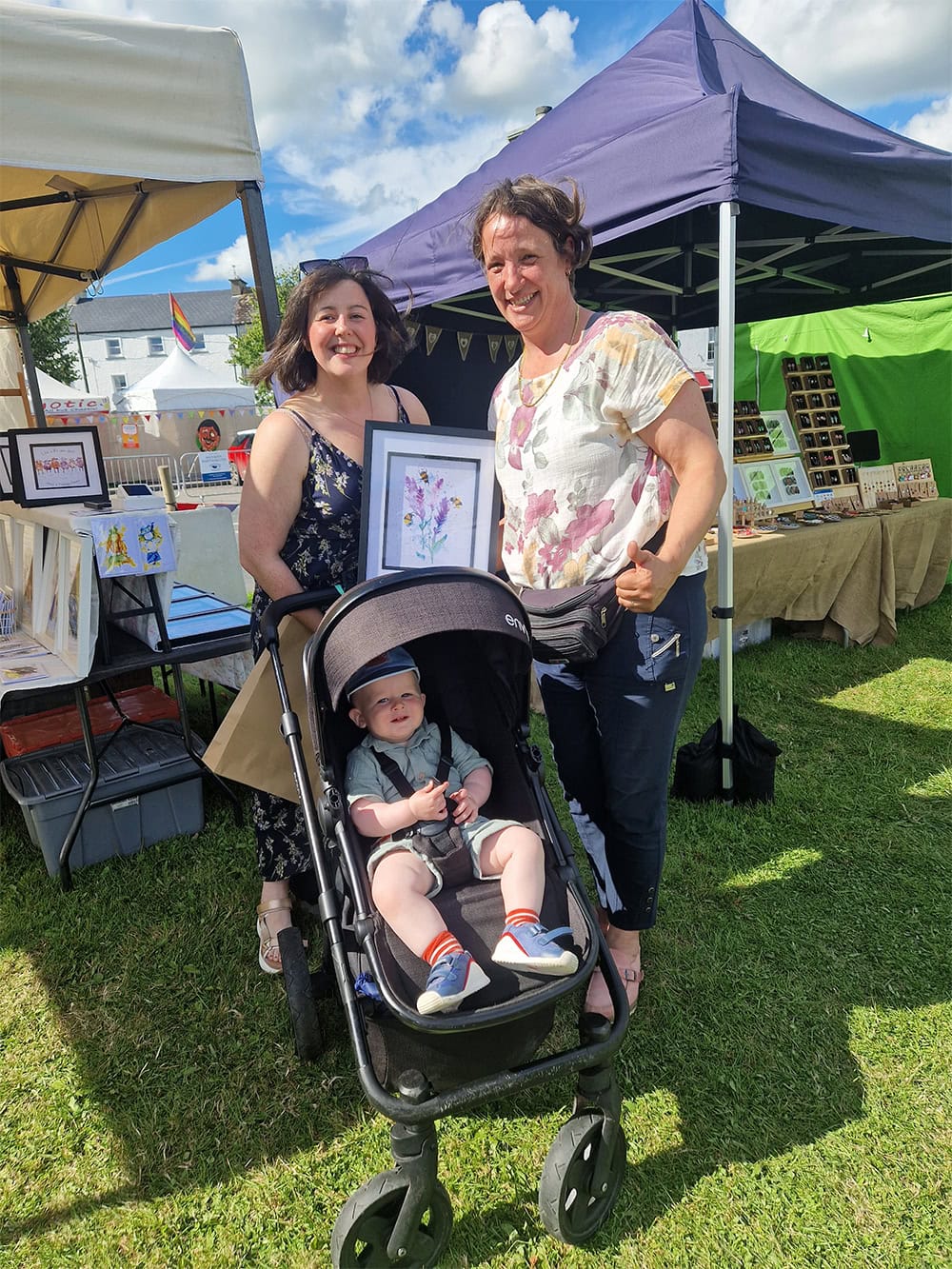 Outdoor art market with smiling people, baby in pram.